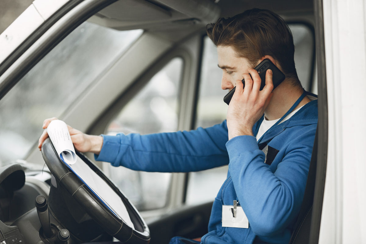 A man in the driver's seat of a van, talking on the phone.